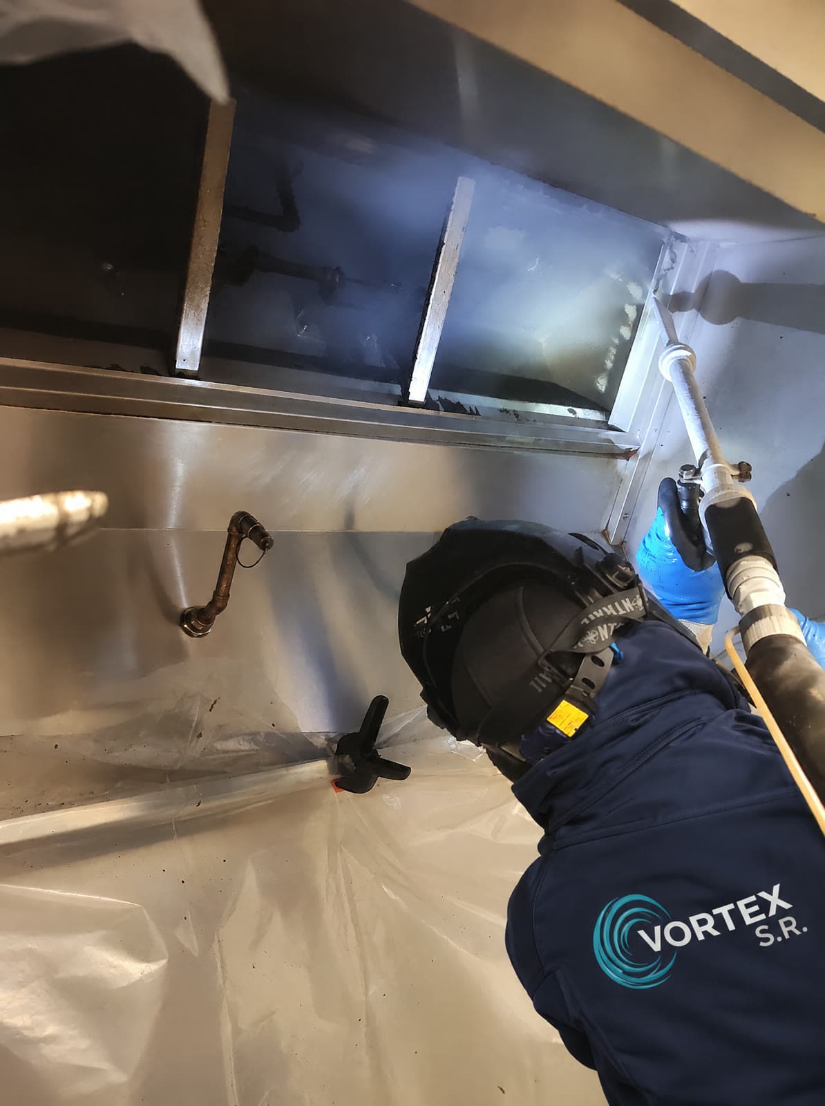 Vortex S.R. medewerker met gelaatsscherm spuit een afzuigkap schoon